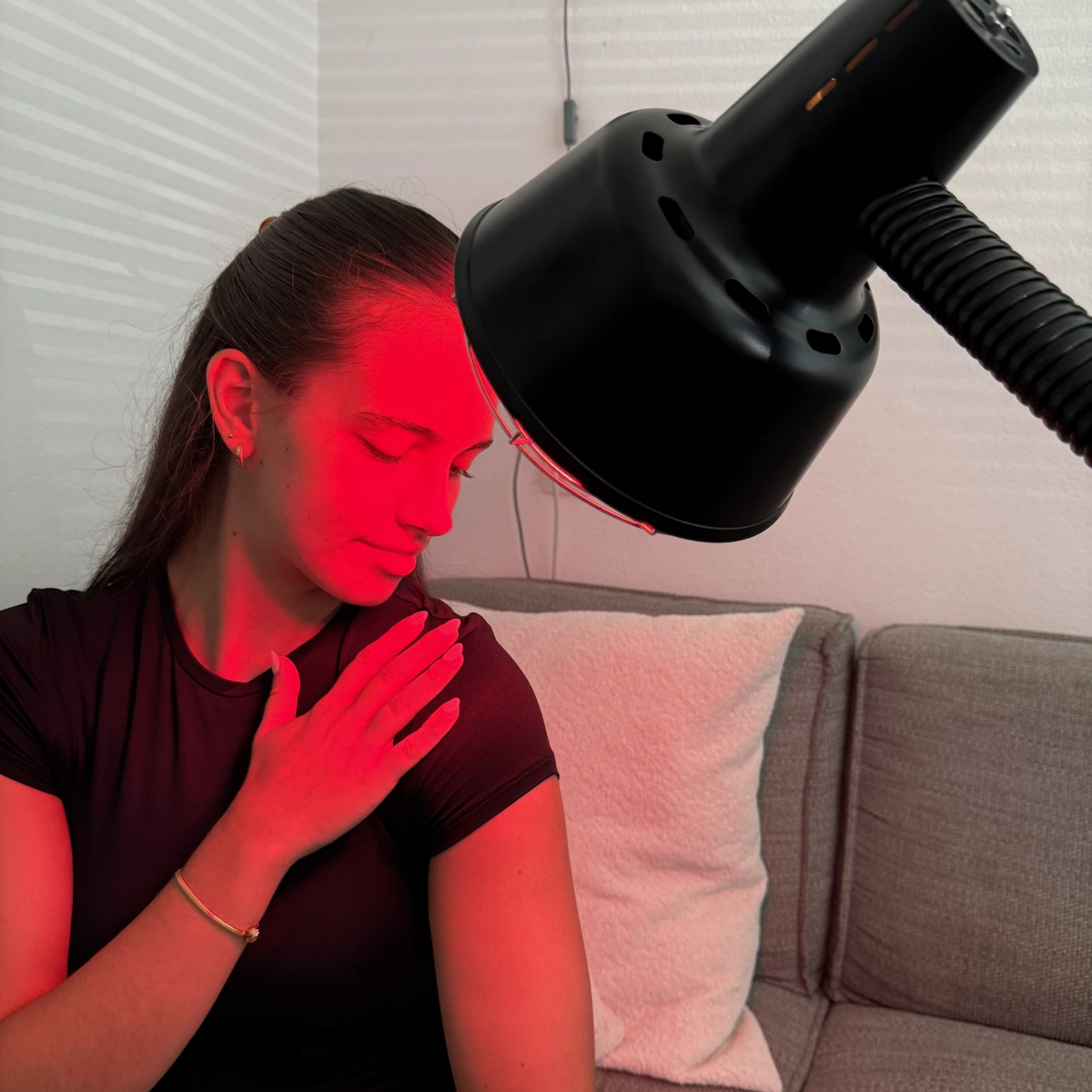 Woman using the Redlight 160 infrared lamp on her shoulder at home on the sofa